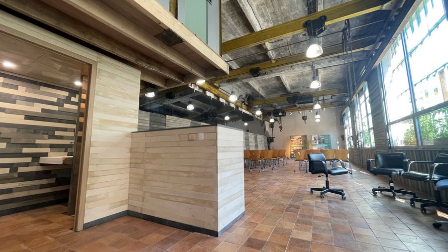 grande salle avec comptoir gauche, chaises au centre, baies vitrées à droite et plafond de poutres métalliques